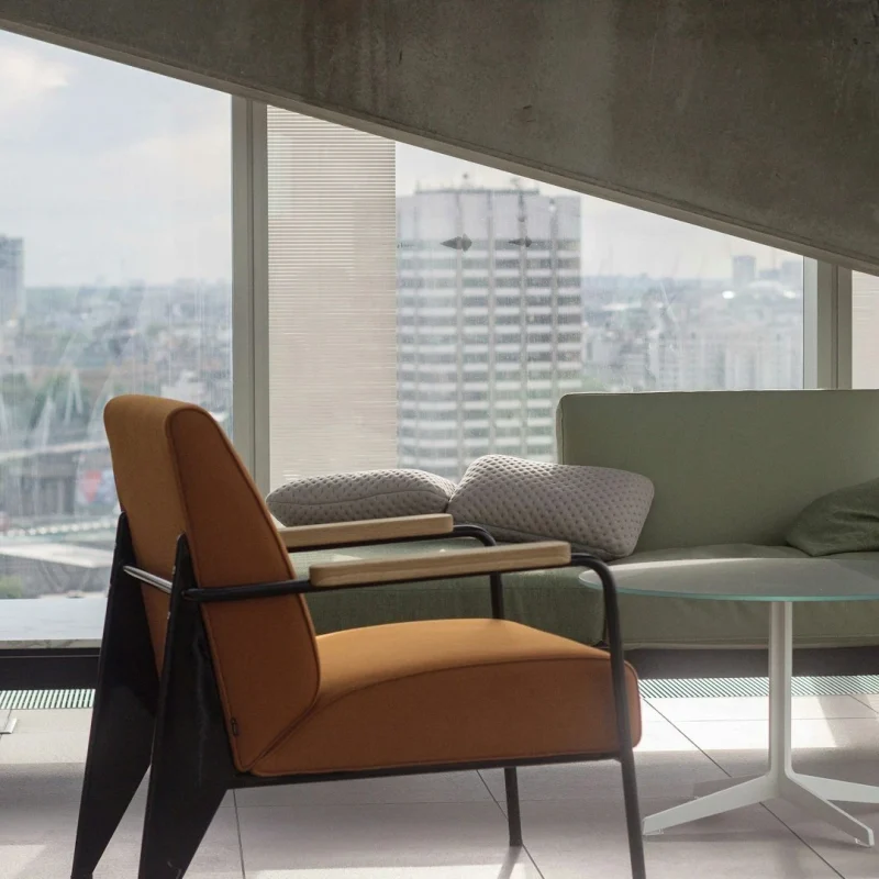 orange-fabric-padded-armchair-with-black-metal-base-near-round-clear-glass-top-table-and-gray-sofa